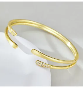 Primer plano detallado del brazalete abierto de metal dorado de doble capa con cristales.