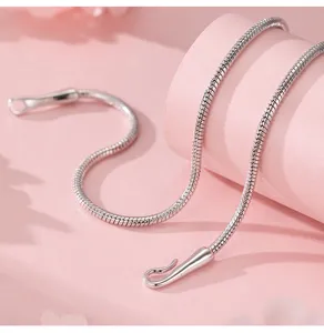 Close-up detail of minimalist silver snake bone chain with unique hook clasp, sleek texture.