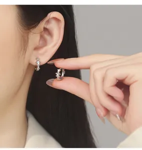 Gros plan détail boucles d'oreilles créoles croix lys argent portées à l'oreille et tenues.