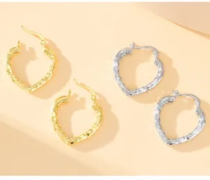 Détail de boucles d'oreilles créoles en forme de cœur, bijoux texturés argent et or.