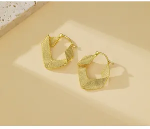 Detailaufnahme gedrehter goldener Creolen mit gewebter Textur und geometrischem Design.