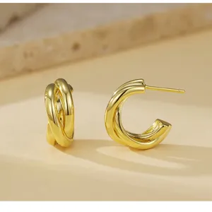 Gedetailleerde close-up van minimalistische dubbele gouden oorbellen met gepolijste metaaltextuur.