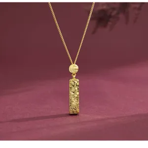Gros plan d'un collier pendentif barre dorée texturée, design élégant et discret.