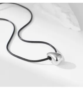 Vue rapprochée détaillée d'un pendentif goutte argenté minimaliste sur cordon noir.