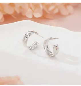 Gros-plan de boucles d'oreilles créoles argentées irrégulières à texture froissée.