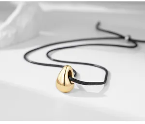 Detail de collier pendentif goutte dore minimaliste sur cordon noir, bijou elegant.