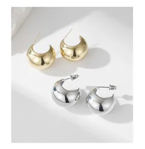 Close-up of stylish C-shaped thick hoop earrings in gold and silver, glossy metal gloss.