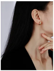 Close-up detail of geometric ridged gold hoop earrings worn on ear, elegant minimalist style.