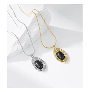Vue détaillée de colliers pendentifs ovales en pierre noire dorée et argentée sur fond.