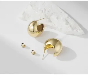 Chunky gold C-shaped hoop earrings detail, minimalist polished metal geometric stud jewelry.