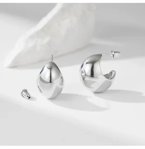 Close-up detail of glossy silver C-shape and teardrop stud earrings, elegant metallic texture.