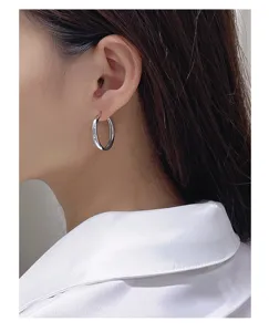 Close-up detail of smooth silver hoop earrings worn on ear, showcasing simple geometric design.