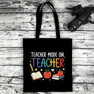 Black canvas tote bag detail featuring colorful teacher text print and school icons.