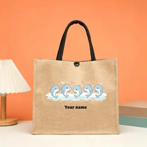 Close-up detail of custom jute tote bag featuring cute cartoon dolphins and personalized name.