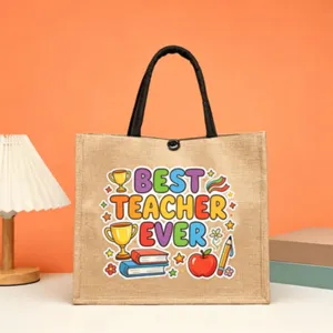 Detailed view of the burlap tote bag with teacher graphic, black handles and snap closure.