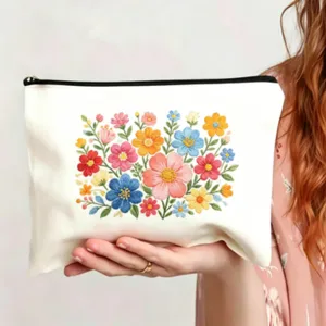Detailansicht des weißen Canvas-Kosmetikbeutels mit bunter Blumenstickerei und schwarzem Reißverschluss.