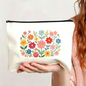 Detailansicht der weißen Canvas-Kosmetiktasche mit farbiger Blumenstickerei und Reißverschluss.