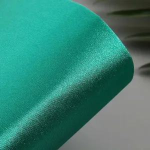 Detailed shot of emerald green stretch satin fabric, smooth glossy texture for elegant wear.