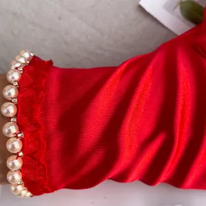 Close-up of elegant red elastic satin glove detail featuring delicate white pearl trim and ruffles.