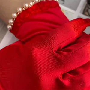 Detail view of red stretch satin gloves with elegant pearl wrist trim for events.