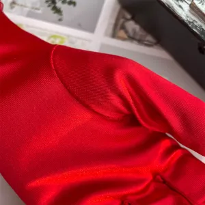 Close-up detail shot of red stretch satin formal gloves, smooth shiny fabric texture.