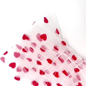 Close-up of white mesh tulle fabric featuring red heart print and smocked ruffles.