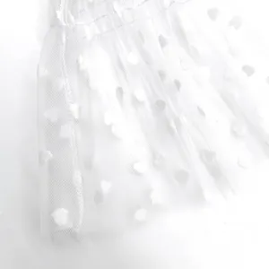 Detailed view of white tulle mesh fabric with flocked dot pattern and gathered ruffle trim.