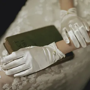 White satin bridal gloves detail shot featuring elegant pearl pendant decoration for wedding.