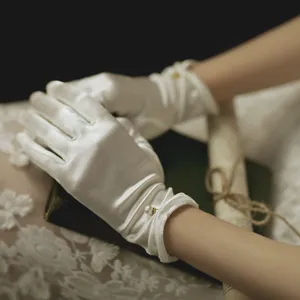 Close-up detail of white satin bridal gloves featuring elegant pearl and bow accent.