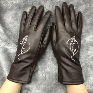Detailed view of brown leather winter gloves featuring delicate white embroidery and warm lining.