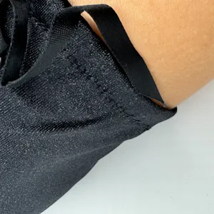 Détail de gant en tissu scintillant noir, coutures fines et ruban pour tenue élégante.