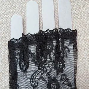 Close-up detail view of black lace fingerless gloves, delicate floral pattern mesh fabric.