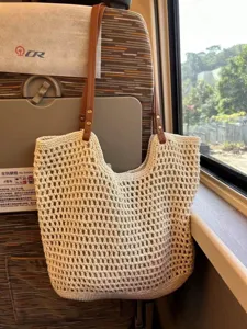 Close-up of the woven straw tote bag with crochet design and leather straps for summer.