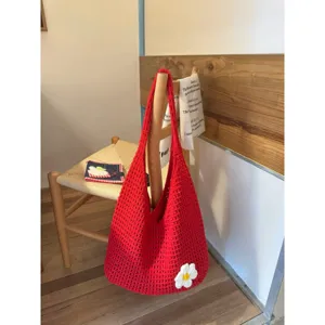 Close-up detail shot of red crochet shoulder bag hanging on wooden chair with flower accent.