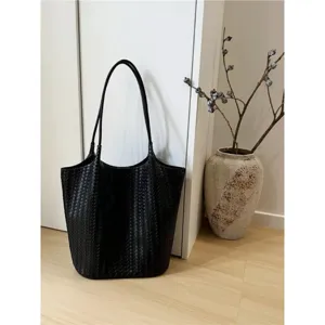 Minimalist black woven leather tote bag detail shot, elegant lifestyle setting on wooden floor.
