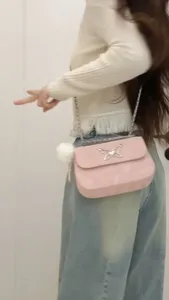 Pink chain shoulder bag detail, elegant butterfly decor and cute pom-pom charm for women.