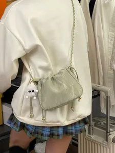 Vue détaillée d'un sac froncé vert clair avec bandoulière chaîne et charm monstre duveteux.