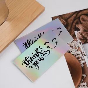 Close-up detail of holographic thank you cards with colorful rainbow reflection on white table.