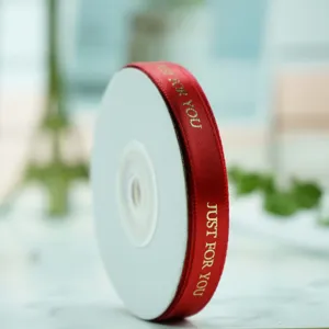 Primo piano di un rotolo di nastro in raso rosso con elegante stampa a caldo dorata per regali.