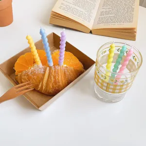 Detailaufnahme von farbenfrohen Spiralgeburtstagskerzen auf einem Croissant und im Glas.