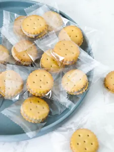 Primer plano de galletas tipo sándwich redondas envueltas individualmente en plato azul, detalle.