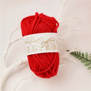 Detailed shot of red craft yarn ball with decorative paper band on white twig prop.