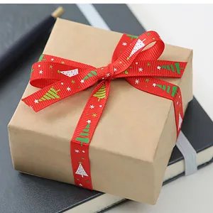 Close-up detail of red Christmas ribbon with festive tree pattern tied neatly on a wrapped gift box.