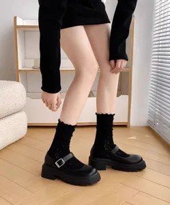 Close-up detail shot of women's black frilly socks and platform Mary Jane shoes indoors.