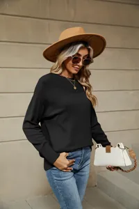 Detail view of a casual women's black knit sweater, showcasing texture, boat neck and ribbed cuffs.