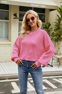 Outdoor street detail view of a casual pink crewneck knit sweater with long sleeves.