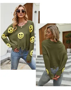 Primo piano del maglione in maglia verde oliva con motivo smiley giallo e orlo sfrangiato.