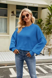 Detailed view of the stylish blue knit sweater worn by a female model in an outdoor cafe scene.