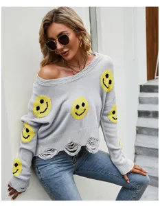 Dettaglio del maglione in maglia grigia strappata con viso smiley giallo e scollo a V.