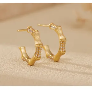 Gros plan détaillé de boucles d'oreilles bambou dorées brossées avec des cristaux.